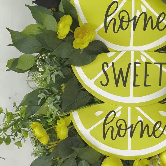 Handmade summer lemon wreath with stacked lemon slice signs reading ‘Home Sweet Home,’ decorated with yellow flowers, faux lemons, greenery, and polka‑dot and lemon‑print ribbons
