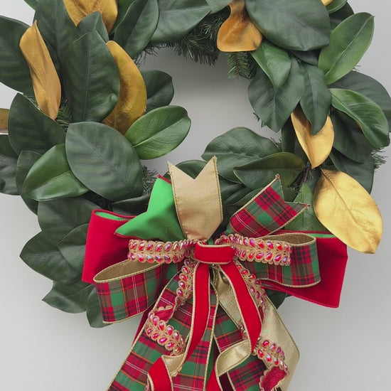 Handmade magnolia Christmas wreath with gold leaves and oversized red green tartan plaid and jeweled holiday bow