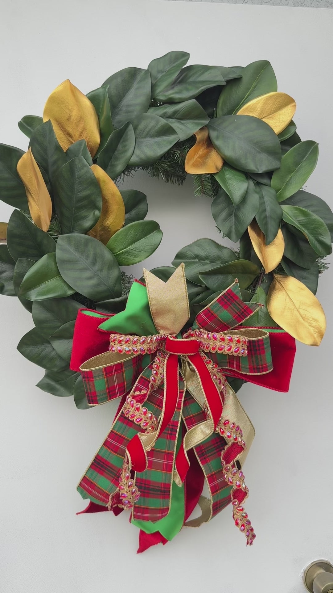 Handmade magnolia Christmas wreath with gold leaves and oversized red green tartan plaid and jeweled holiday bow