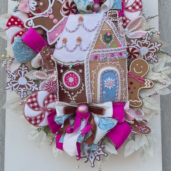 Sugarplum Gingerbread Cottage Christmas Wreath with pastel gingerbread house, pink and blue bows, poinsettias and Norfolk fir greenery.