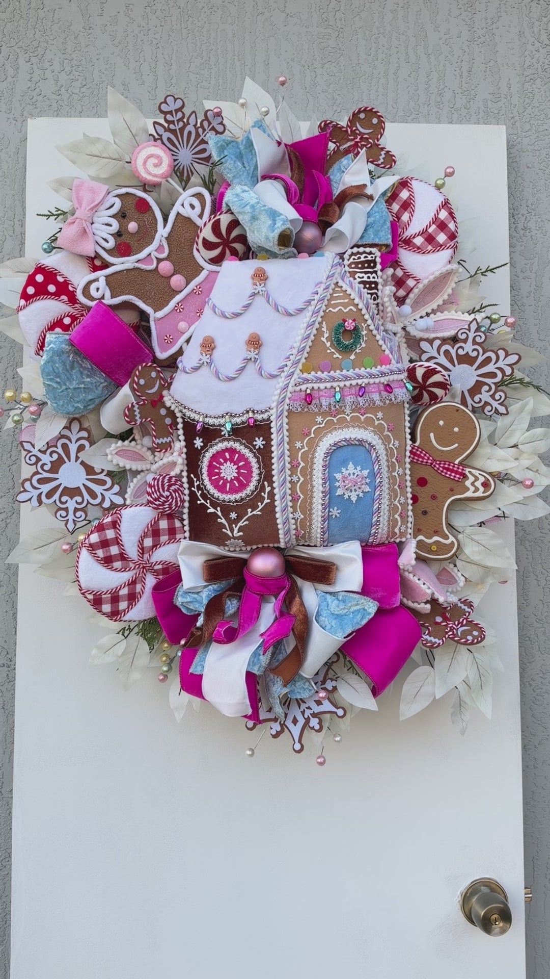 Sugarplum Gingerbread Cottage Christmas Wreath with pastel gingerbread house, pink and blue bows, poinsettias and Norfolk fir greenery.