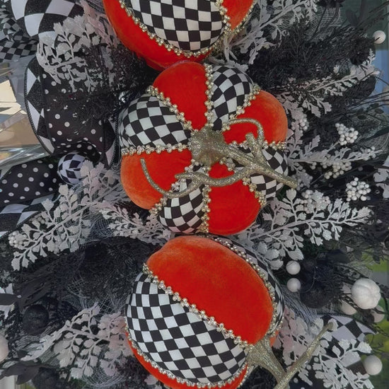 Handmade fall wreath with black‑and‑white checkered pumpkins, gold stems, and black, white, and silver foliage with patterned ribbons on a dark door
