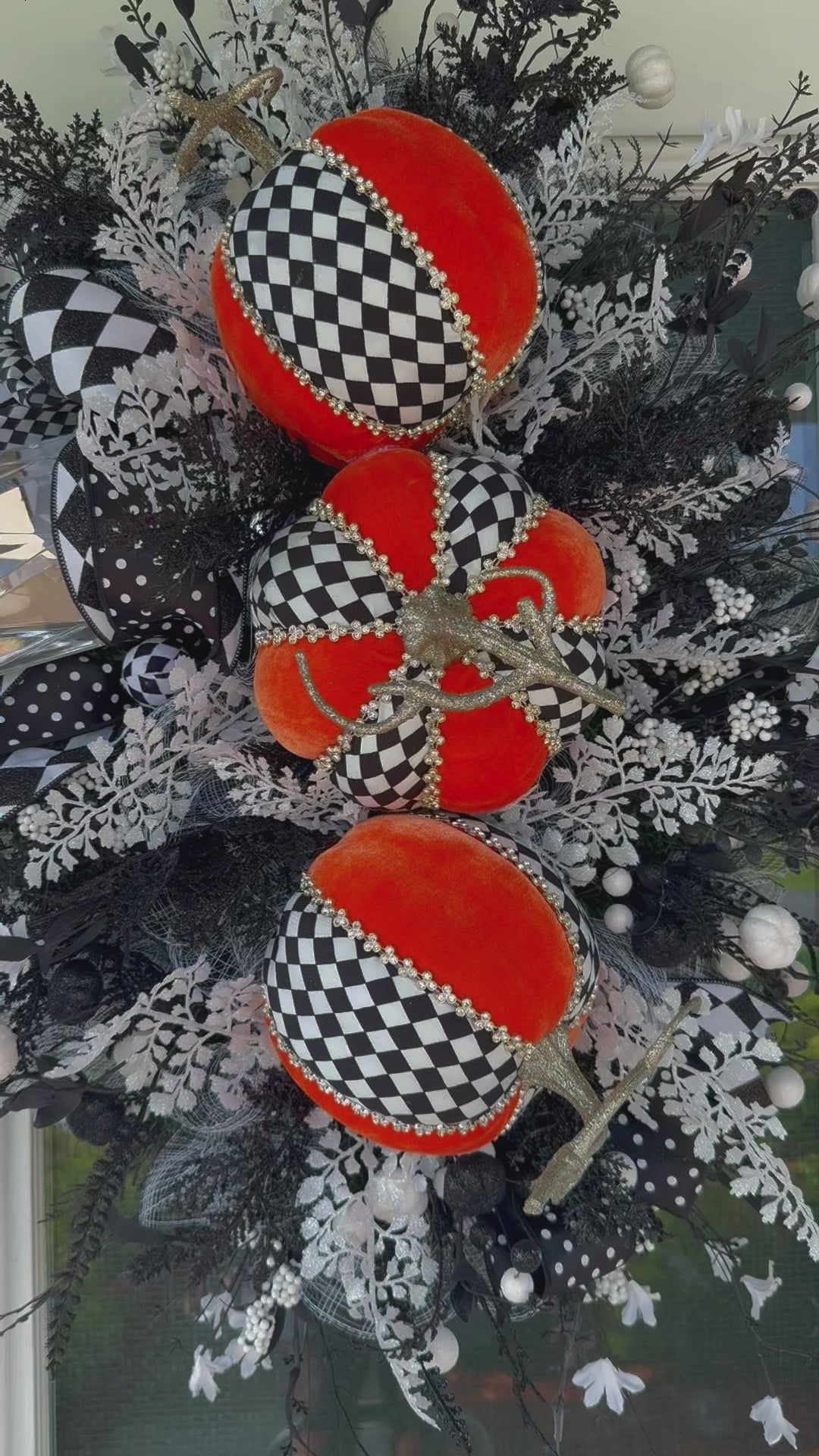 Handmade fall wreath with black‑and‑white checkered pumpkins, gold stems, and black, white, and silver foliage with patterned ribbons on a dark door